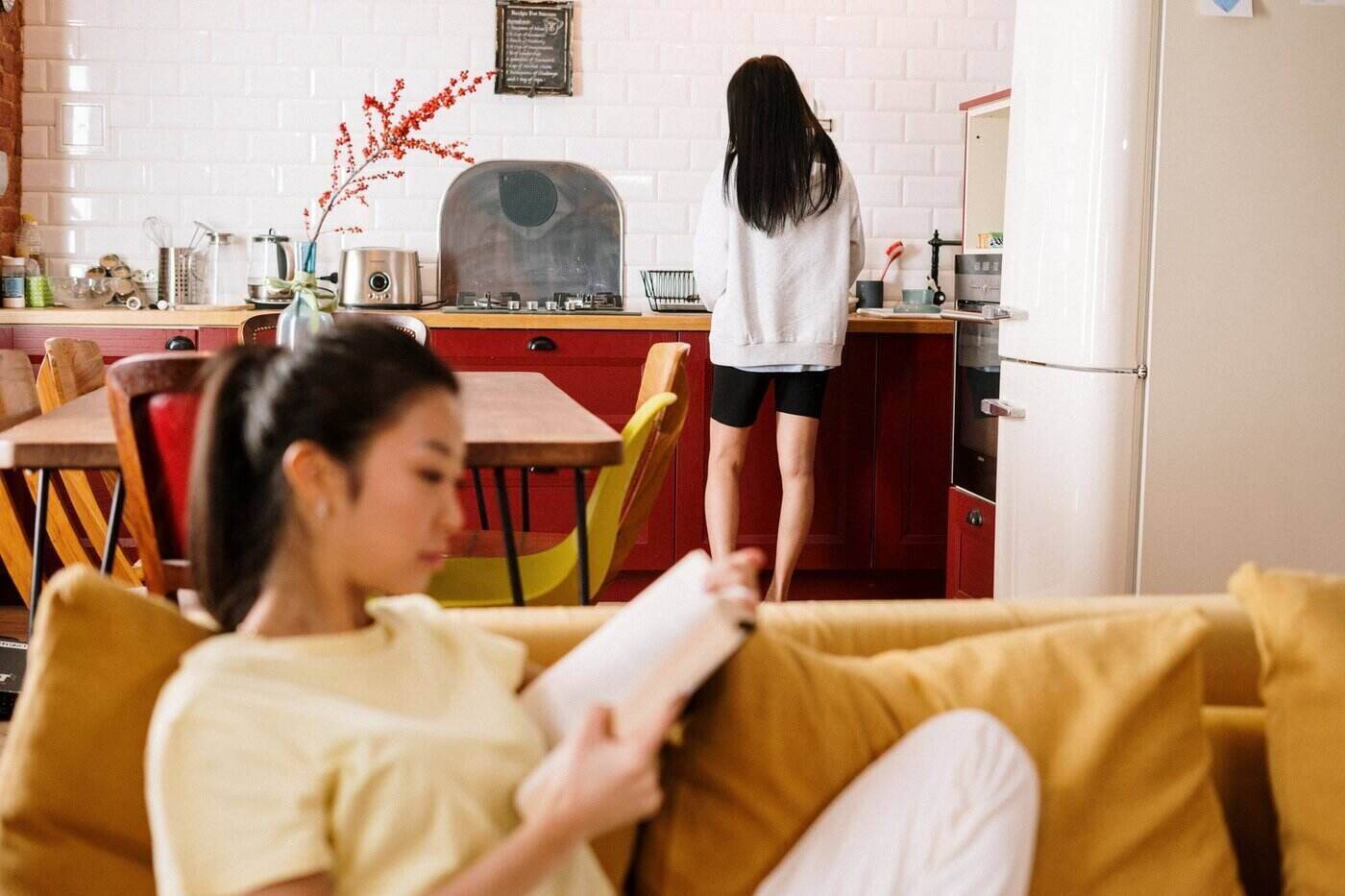 How Co-Living Can Cut Your Carbon Footprint 4 Woman reading on couch while another woman cooks - how co-living can cut your carbon footprint