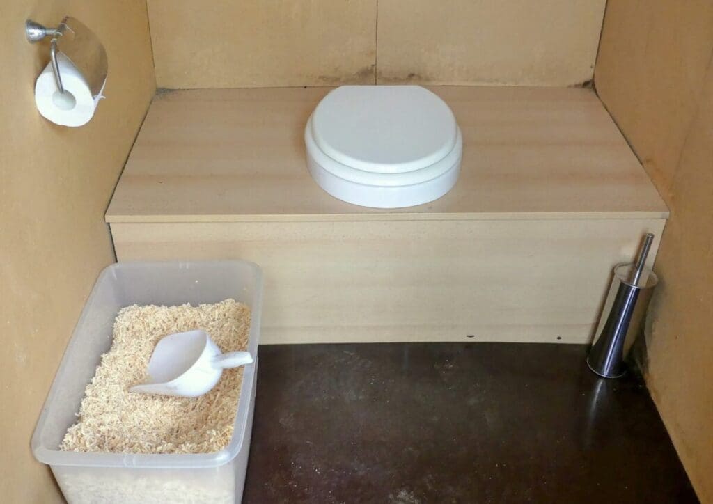 Composting toilet in wood structure with wood chips beside - composting toilets: taking responsibility for our own waste
