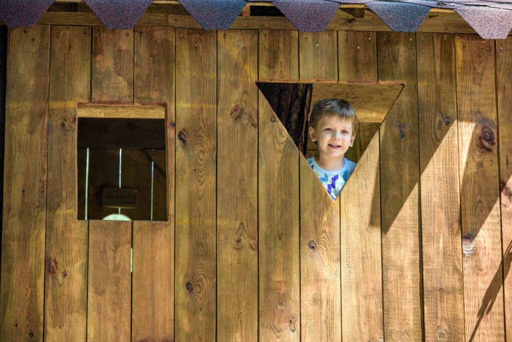 Boy looking out from diy wood playhouse for kids